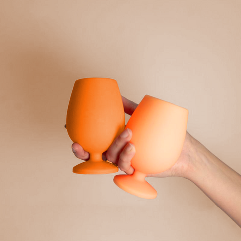 Two orange silicone cups held by a hand against a beige background